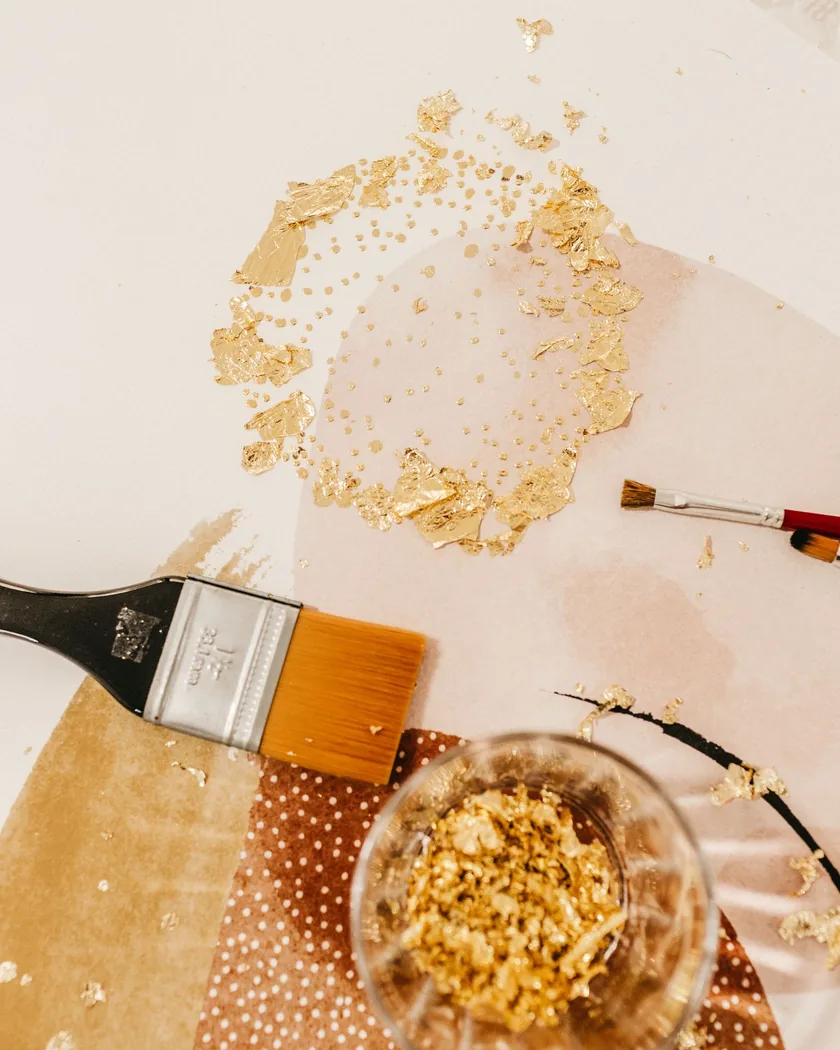 Restos de pan de oro, pinceles de dorador y un recipiente con recortes de oro sobre una mesa de trabajo